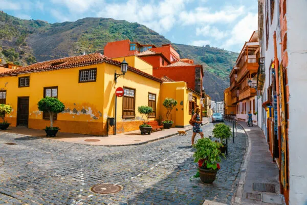 Een gekasseide straat in het kuststadje Garachico, geflankeerd door felgele en oranje traditionele huizen tegen een achtergrond van groene bergen op Tenerife.