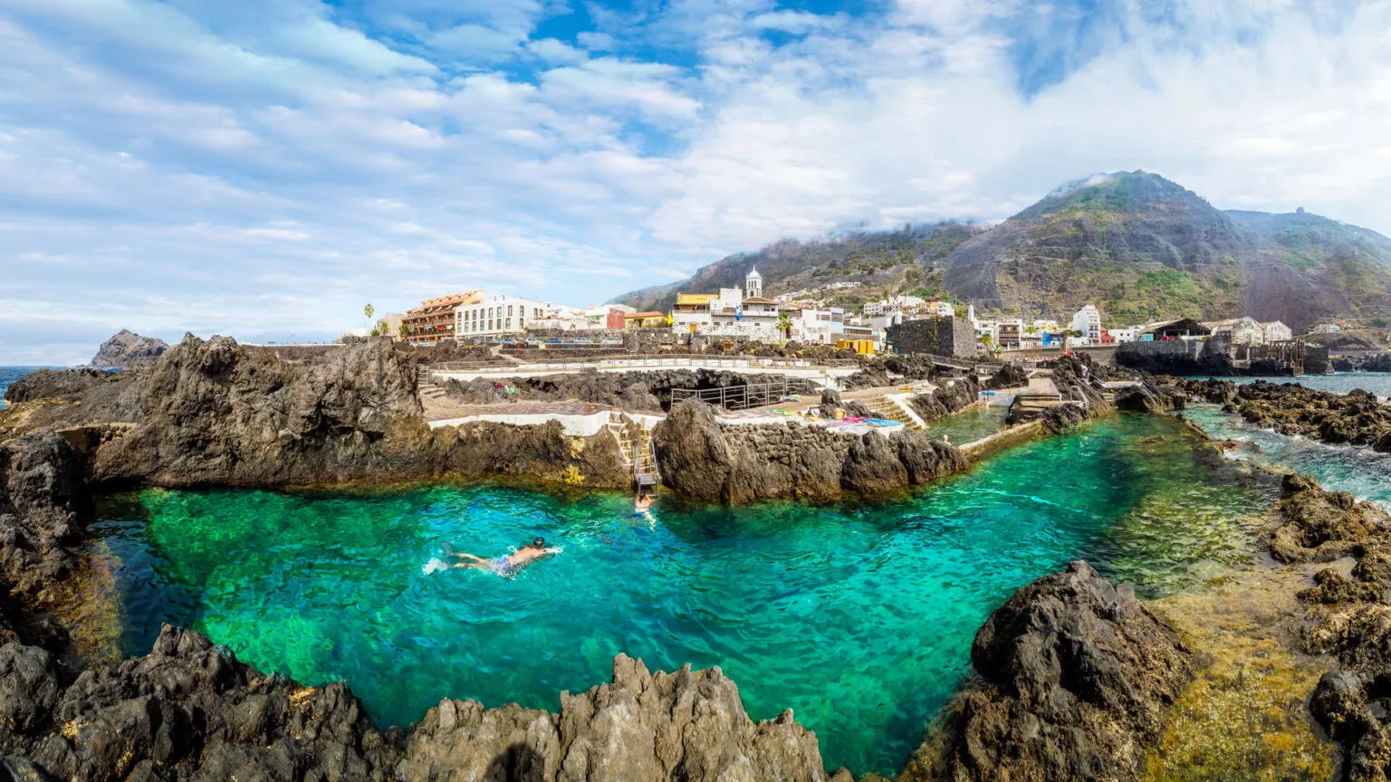Helder turkoois water in de vulkanische rotsbaden van El Caletón met op de achtergrond het kuststadje Garachico op Tenerife