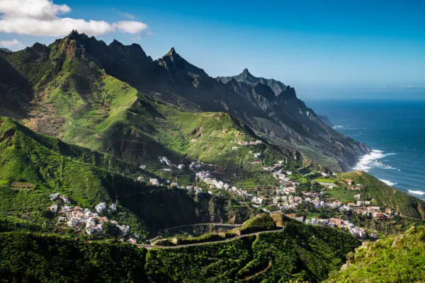 Panoramisch uitzicht over de steile, groene bergen van het Anaga-gebergte met het witte dorp Taganana tegen de helling en de oceaan op de achtergrond op Tenerife