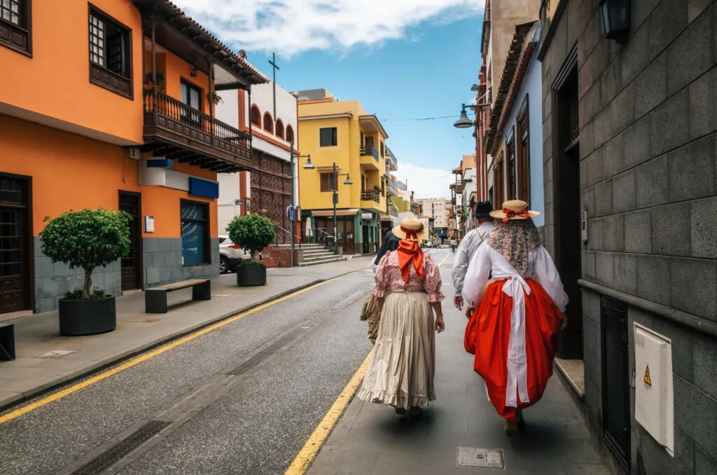 Twee mensen in kleurrijke traditionele kleding lopen door een schilderachtige straat met historische gebouwen op Tenerife.