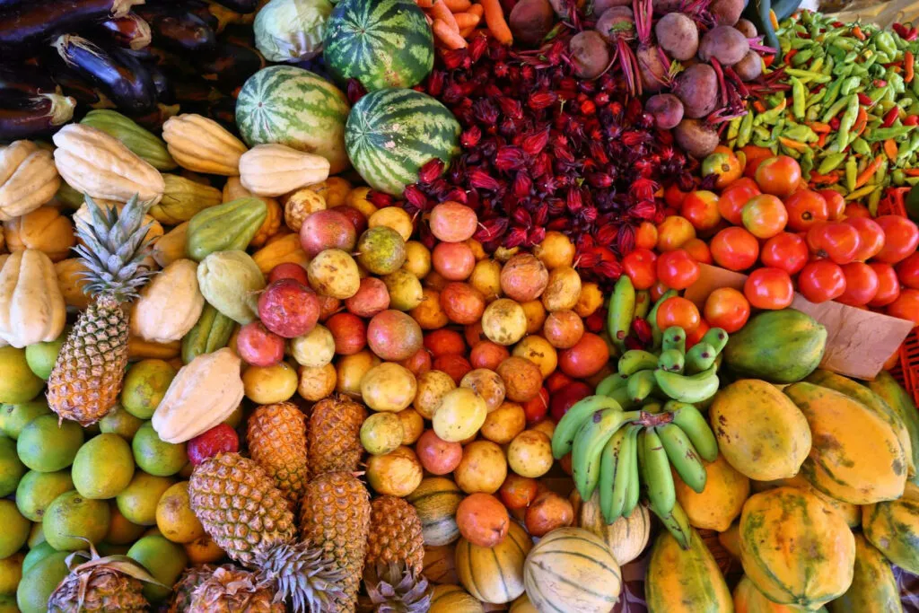 Een kleurrijke verzameling vers tropisch fruit zoals watermeloenen, bananen en ananassen ligt uitgestald op een Caribische markt.