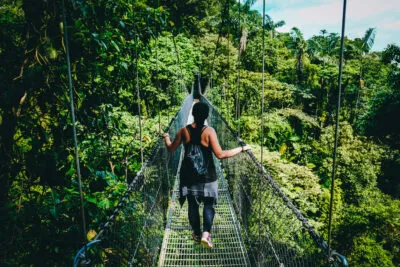 Een vrouwelijke reiziger wandelt over een hangbrug tussen het weelderige groen van de jungle in Costa Rica