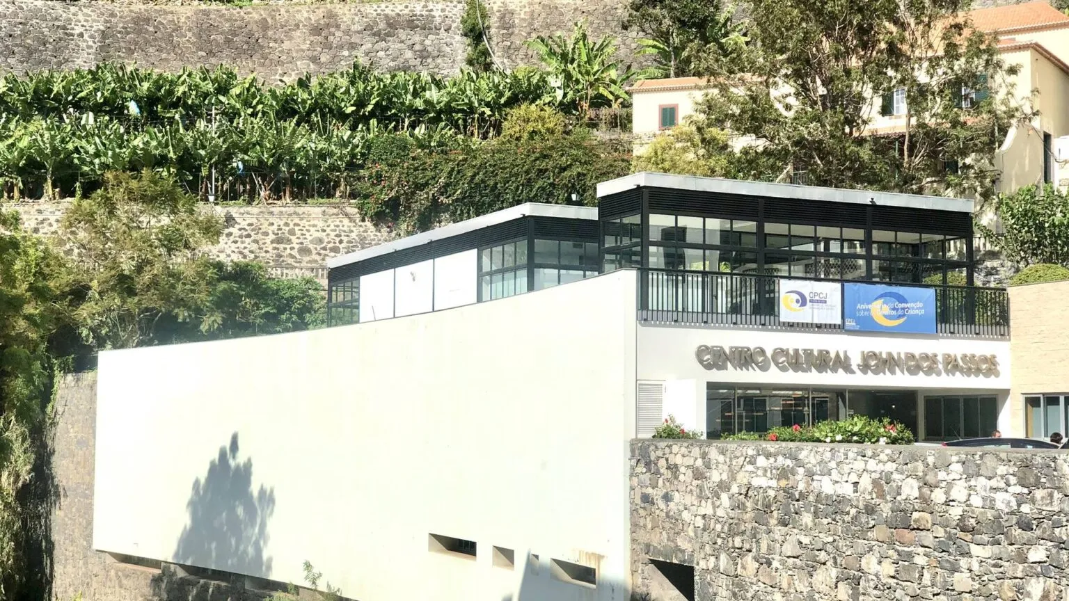 Een modern wit gebouw met grote raampartijen voor digital nomads, gelegen aan de voet van een met groen begroeide heuvel op Madeira.