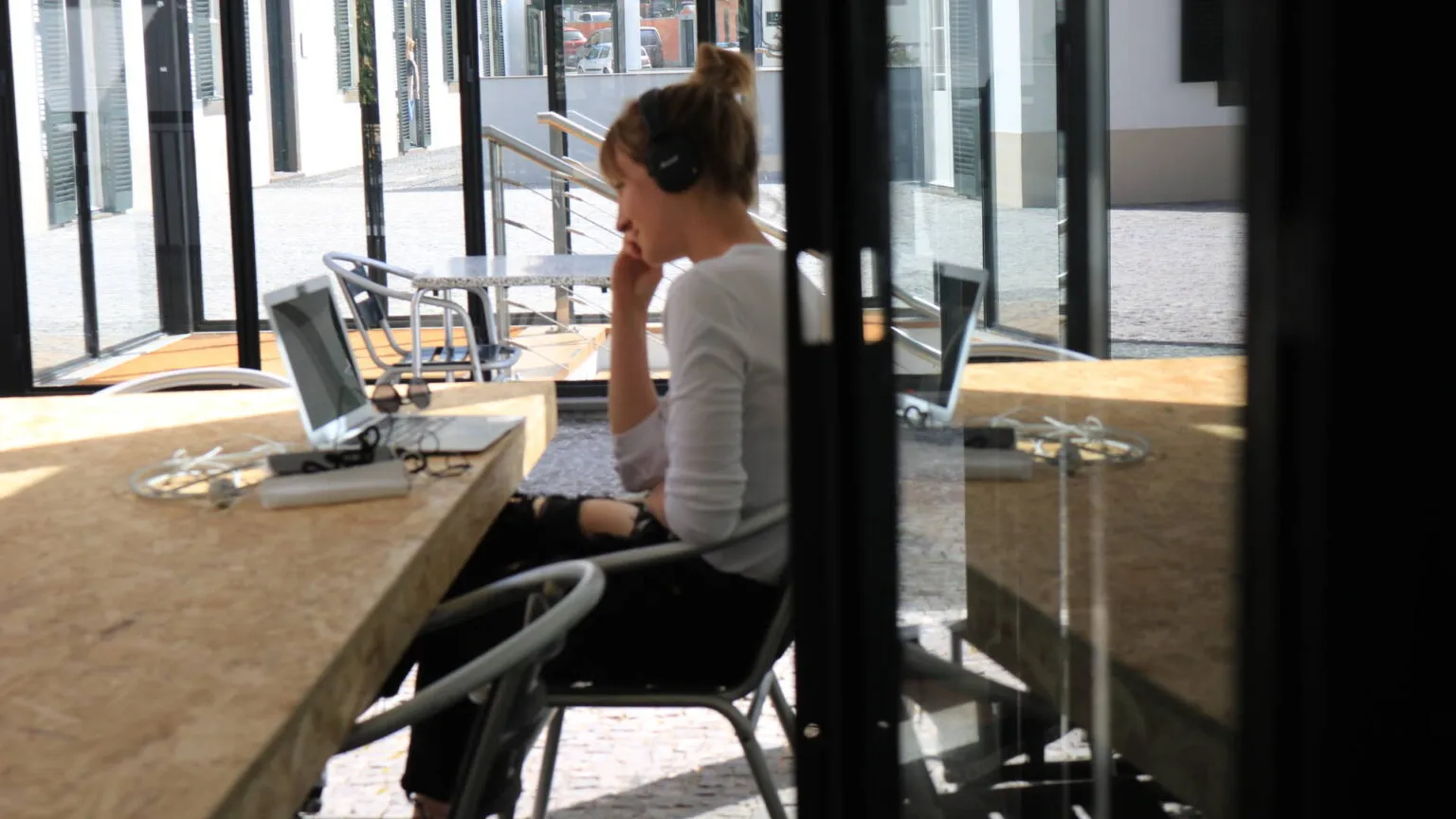 Zijaanzicht van een vrouw die met een koptelefoon op aan een bureau zit te werken in een moderne, lichte kantoorruimte.