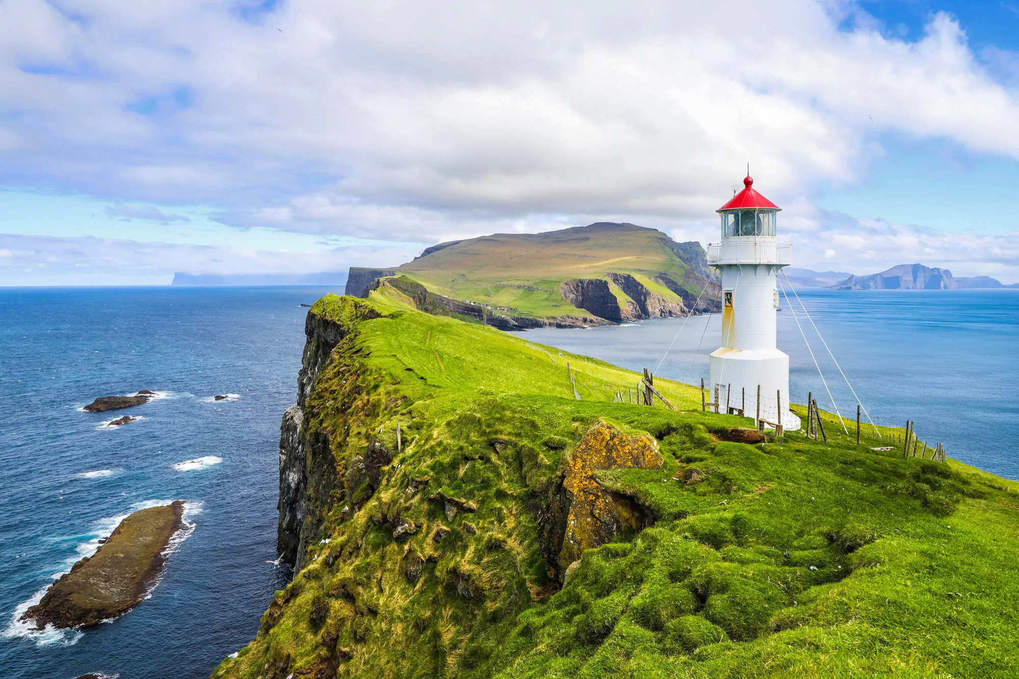 Rood-witte vuurtoren in een groen landschap aan de kust van het eiland Mykines