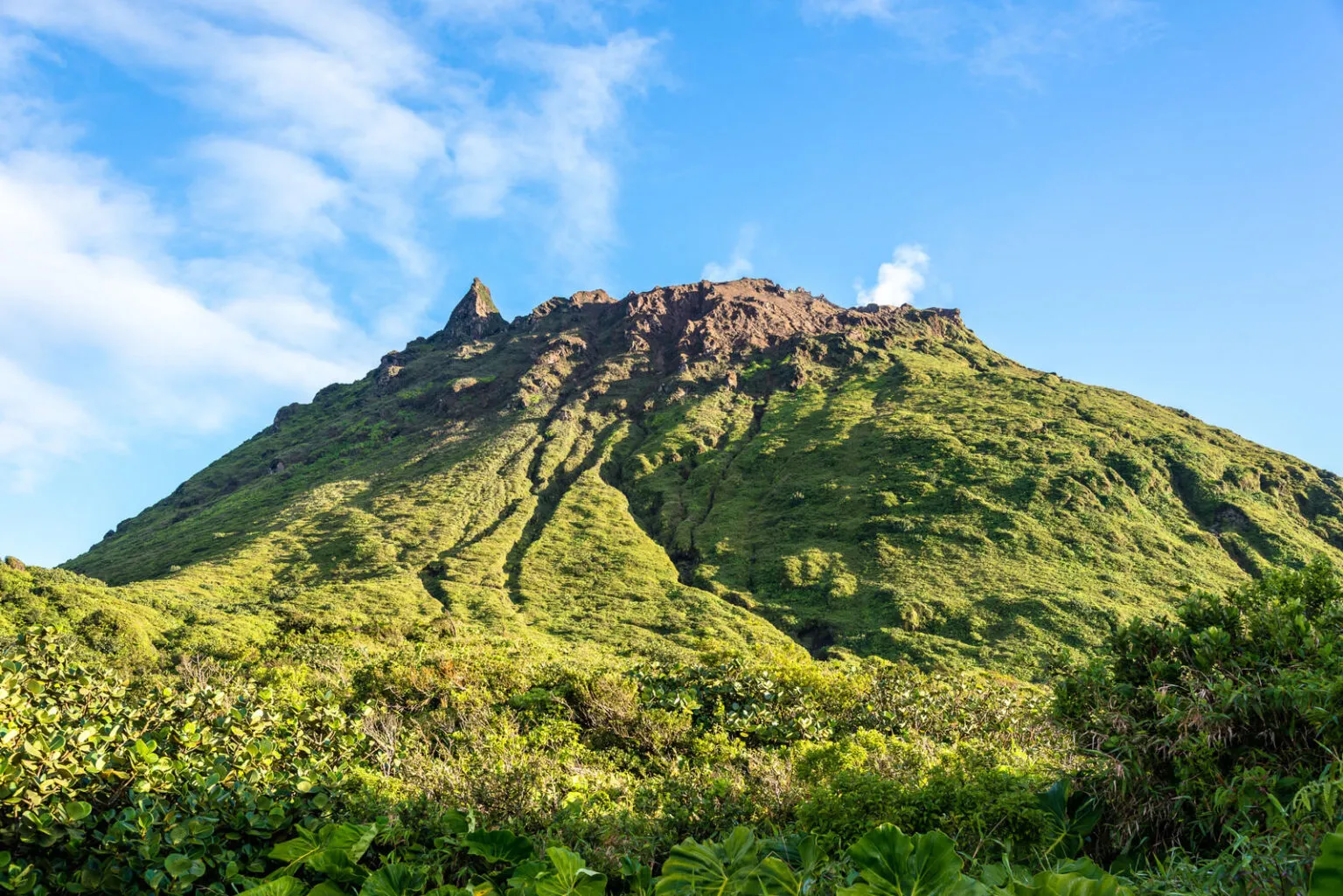 Zicht op de groene, steile hellingen en de rotsachtige top van de actieve vulkaan La Grande Soufrière tegen een heldere blauwe lucht in het zuiden van Basse-Terre op Guadeloupe.