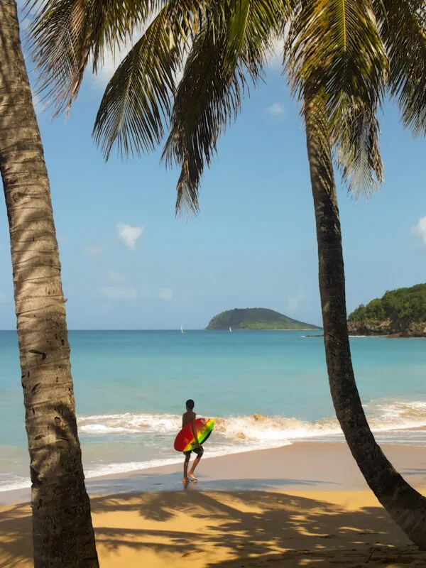 Een local loopt met een surfboard over het strand van Grande-Anse op Basse-Terre.