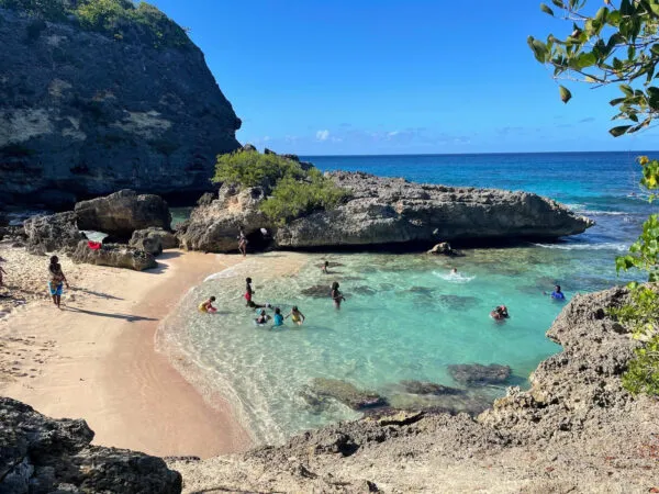 Aanzicht op een kleine, door rotsen omsloten baai met een zandstrand en zwemmers in helder turquoise water op Grande-Terre in Guadeloupe.
