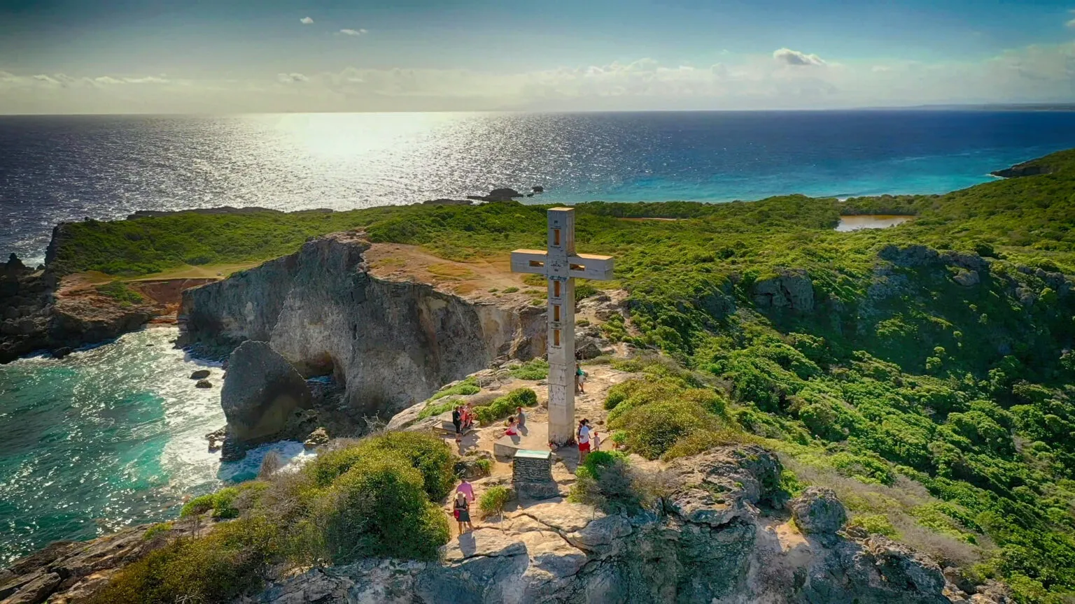 Luchtfoto van een groot houten kruis op de rotsachtige kaap van Pointe des Châteaux op Grande-Terre, Guadeloupe, waar wandelaars genieten van het panorama over de ruige kust en de Atlantische Oceaan.