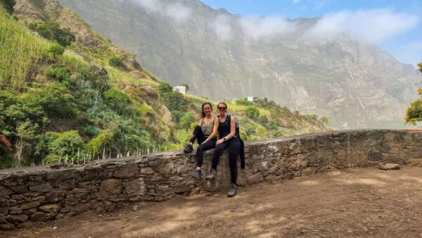 Twee wandelaars zitten op een lage stenen muur en kijken uit over het weelderige groene berglandschap van Santo Antao in Kaapverdië.