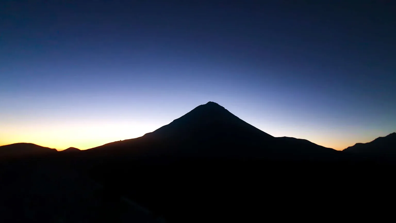 Donker silhouet van de vulkaan Pico do Fogo tegen een kleurrijke oranje en blauwe lucht bij zonsopkomst op Fogo.