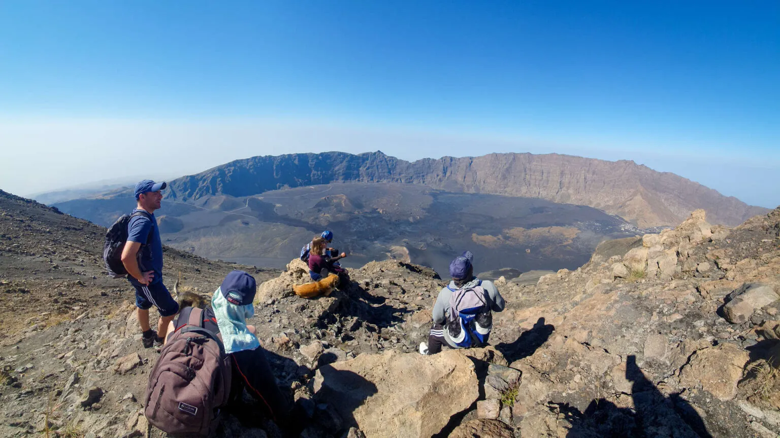 Wandelaars rusten uit op een rotsachtige bergtop met uitzicht over de enorme vulkaankrater op Fogo in Kaapverdië.