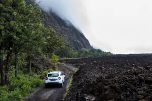 Een 4x4 auto rijdt over een weg aan de voet van vulkaan Fogo, met aan de rechterzijde een zwart lavalandschap