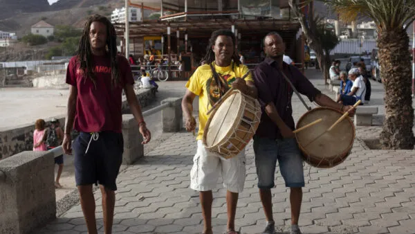 Drie Kaapverdische mannen lopen over een boulevard, waarvan er twee traditionele trommels bespelen op Kaapverdië.