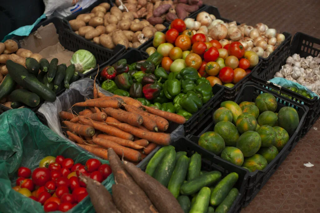 Kratten vol kleurrijke verse groenten en fruit, zoals wortels, tomaten, limoenen en komkommers, uitgestald op een markt op Kaapverdië.
