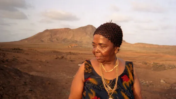 De Kaapverdische zangeres Cesária Évora staat voor een droog berglandschap op Kaapverdië.