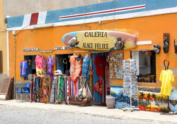 Een geel geverfde souvenirwinkel met kleding, surfplanken en lokale kunstwerken langs de straat in Santa Maria op Sal, Kaapverdië.