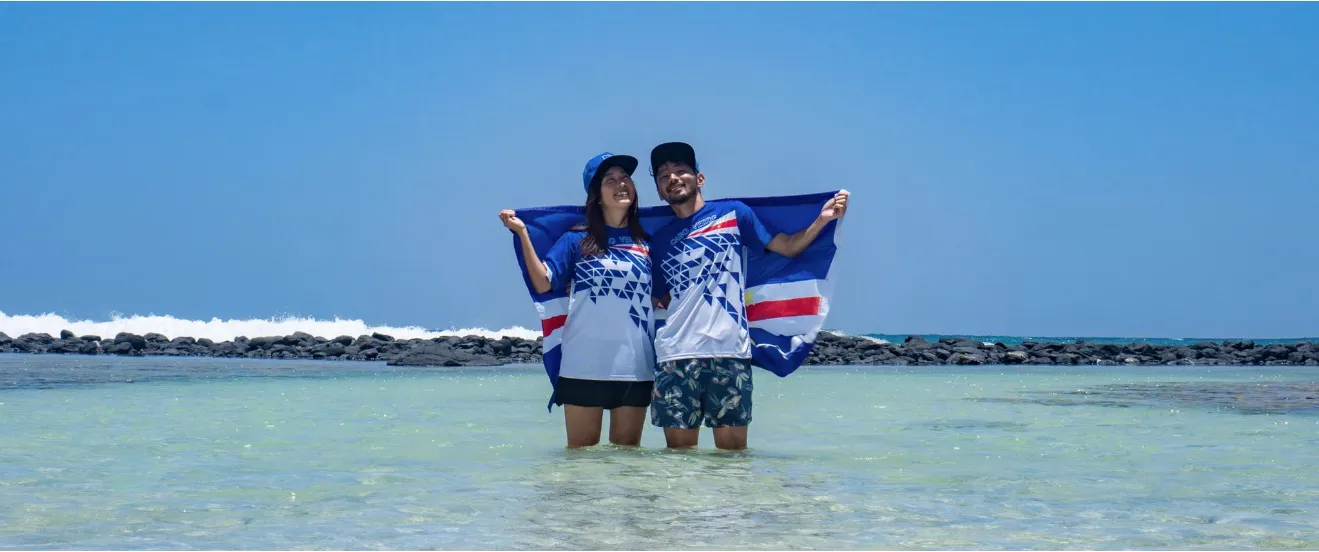 Stel staat glimlachend in het heldere, ondiepe turquoise zeewater en houdt de vlag van Kaapverdië omhoog op het eiland Sal