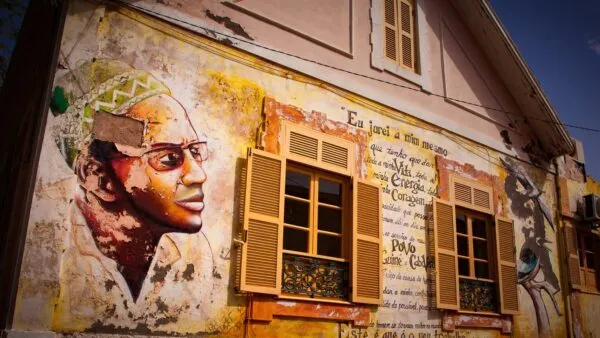 Kleurrijke muurschildering van Amílcar Cabral en geschreven tekst op de gevel van een koloniaal gebouw met houten luiken in Praia, Santiago.