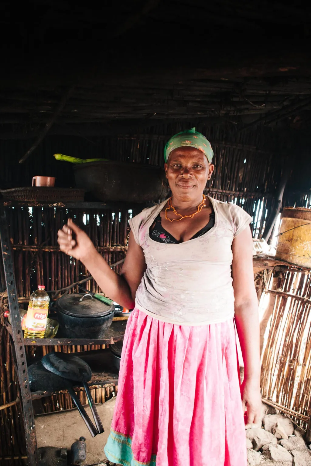 Vrouw uit de Rabelados-gemeenschap met een groene hoofddoek en opvallende roze rok, staand in een traditionele woning met houten wanden op het eiland Santiago in Kaapverdië