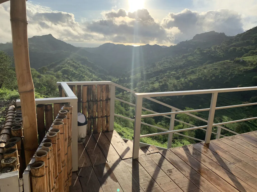 Een houten balkon en terras kijken uit over een groen, bergachtig dal op het eiland Santiago in Kaapverdië bij zonsondergang.