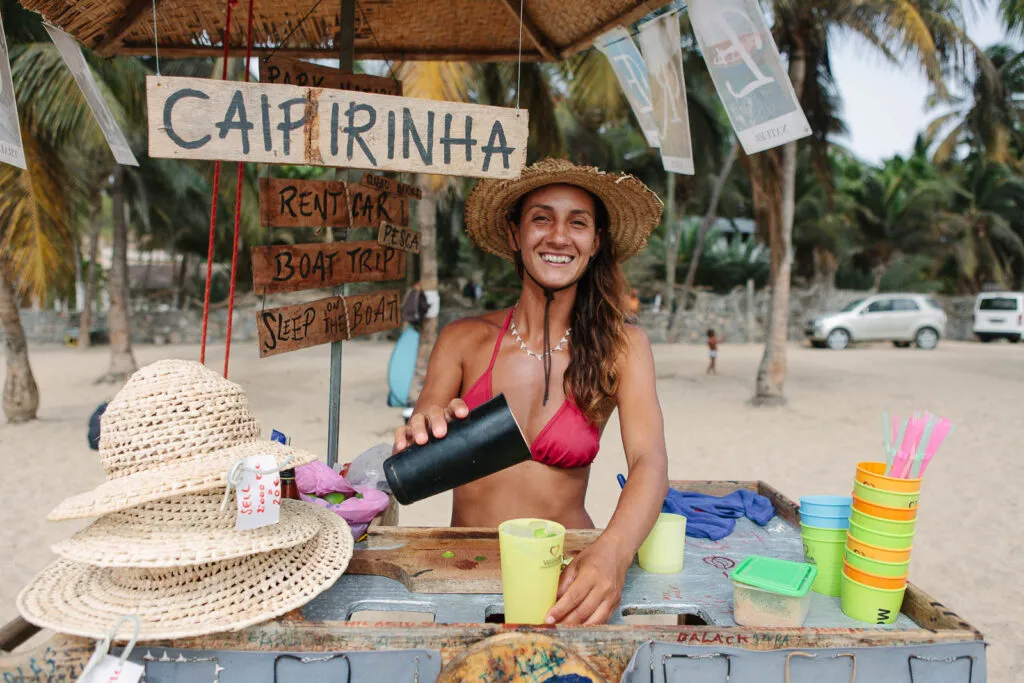 Een vrouw schenkt een caipirinha in bij een strandbarretje op het eiland Santiago