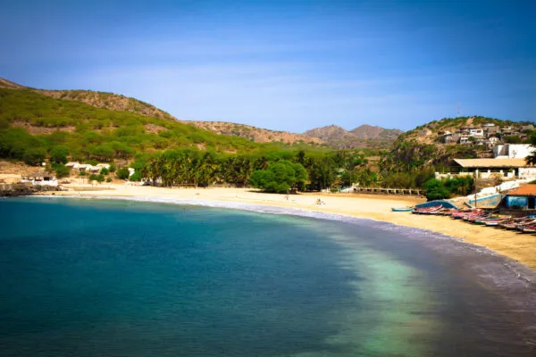 Een zandstrand in een baai met kalm turquoise water, palmbomen en groene bergen in Tarrafal op het eiland Santiago, Kaapverdië.