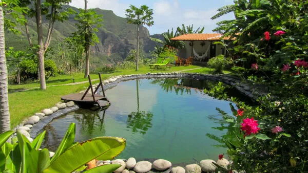 Een natuurlijk zwembad omringd door palmbomen, bloemen en uitzicht op de bergen bij een eco-lodge in de Paúl-vallei op Santo Antão, Kaapverdië.