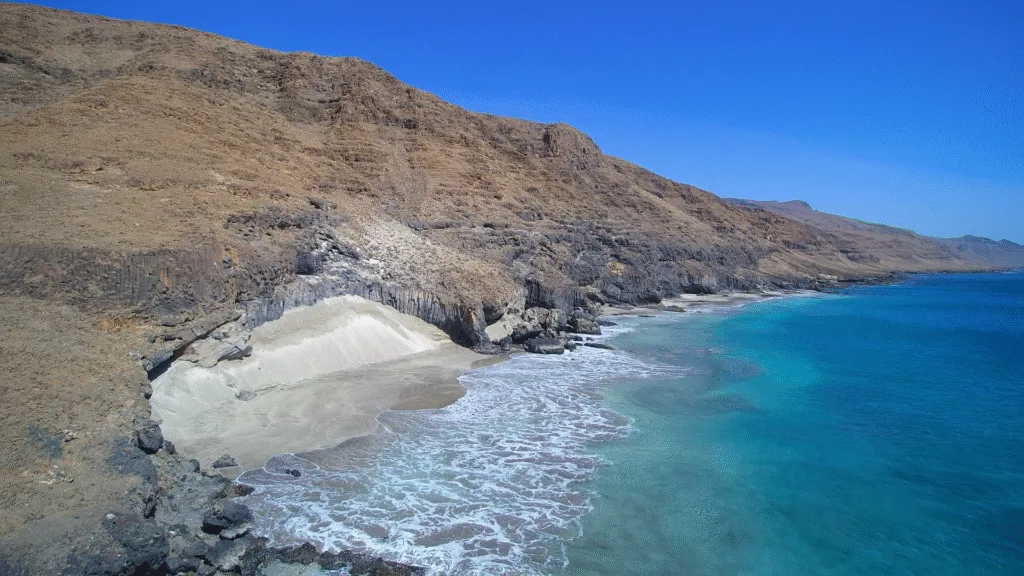 Afgelegen zandstrand van Praia Baixo das Rochas met helder turquoise water omsloten door droge, ruige rotskliffen op het eiland São Nicolau in Kaapverdië