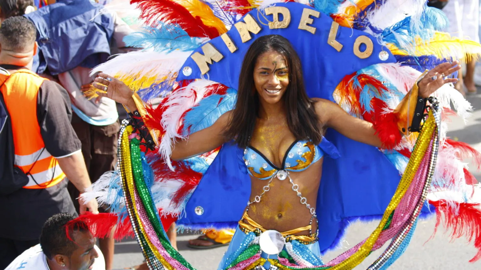 Een vrouw in een kleurrijk carnavalscostuum met een hoofdtooi met de tekst Mindelo danst tijdens het carnaval op São Vicente in Kaapverdië.