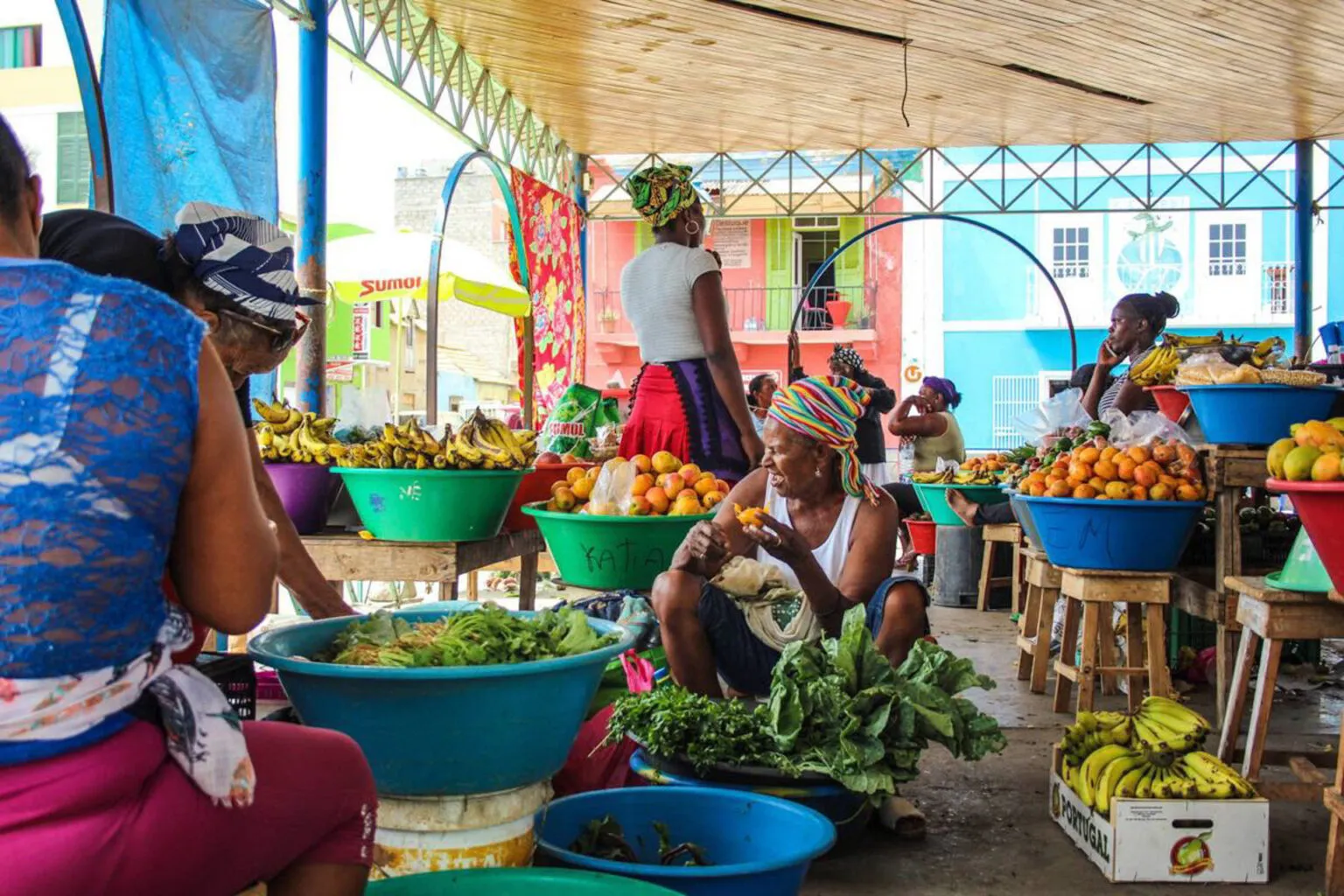 Lokale marktkoplopers en verkopers achter kleurrijke schalen vol vers fruit en groenten op een overdekte markt in São Vicente, Kaapverdië.
