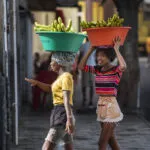 Twee vrolijke jonge lokale vrouwen lopen met grote bakken bananen op hun hoofd op straat op het eiland São Vicente, Kaapverdië