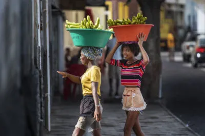 Twee vrolijke jonge lokale vrouwen lopen met grote bakken bananen op hun hoofd op straat op het eiland São Vicente, Kaapverdië