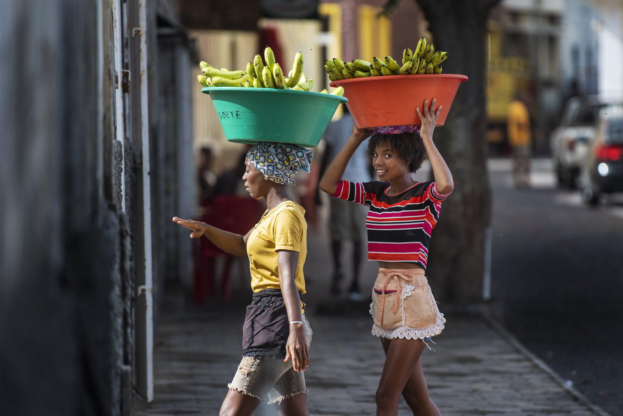 Twee vrolijke jonge lokale vrouwen lopen met grote bakken bananen op hun hoofd op straat op het eiland São Vicente, Kaapverdië