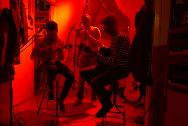 Drie muzikanten maken samen muziek met gitaren en een microfoon in een intieme, rood verlichte ruimte op het eiland São Vicente in Kaapverdië