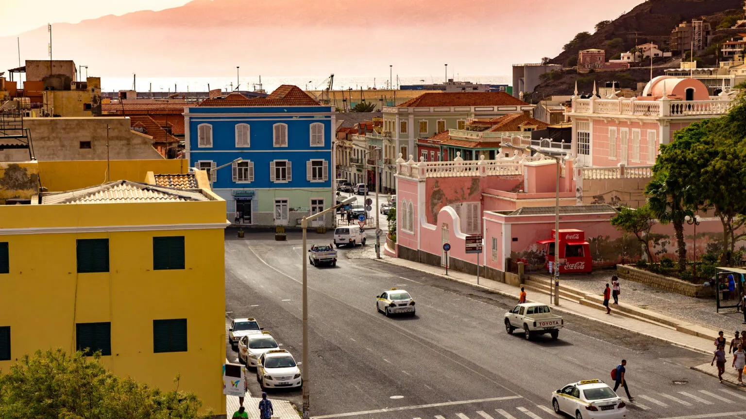 Een straatbeeld in Mindelo met kleurrijke geel, blauw en roze geverfde koloniale gebouwen langs een geasfalteerde weg op het eiland São Vicente in Kaapverdië.