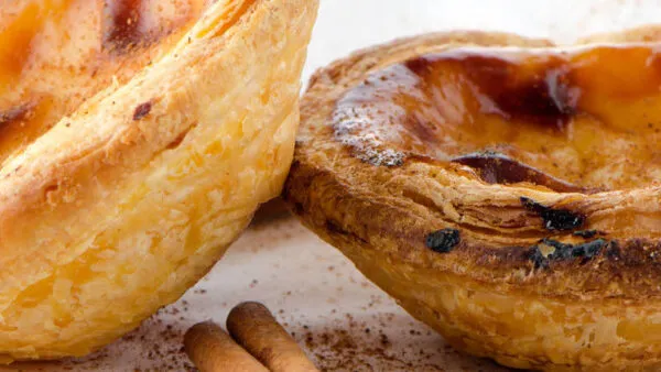 Close-up van goudbruin gebakken pastéis de nata custardpasteitjes met kaneel op de voorgrond.