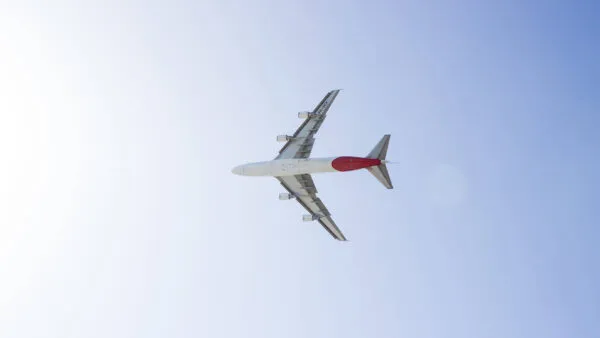 Onderaanzicht van een passagiersvliegtuig met een rode staart dat door een helderblauwe lucht vliegt op weg naar Kaapverdië.