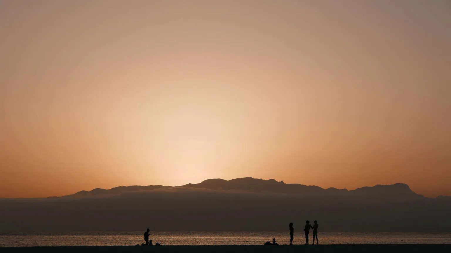 Silhouetten van mensen op het strand tijdens een warme zonsondergang met bergen aan de horizon op São Vicente, Kaapverdië.