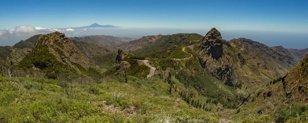 Weids panoramisch uitzicht over de groenbegroeide bergen en opvallende rotsformaties van Nationaal Park Garajonay, met de vulkaan El Teide in de verte op La Gomera