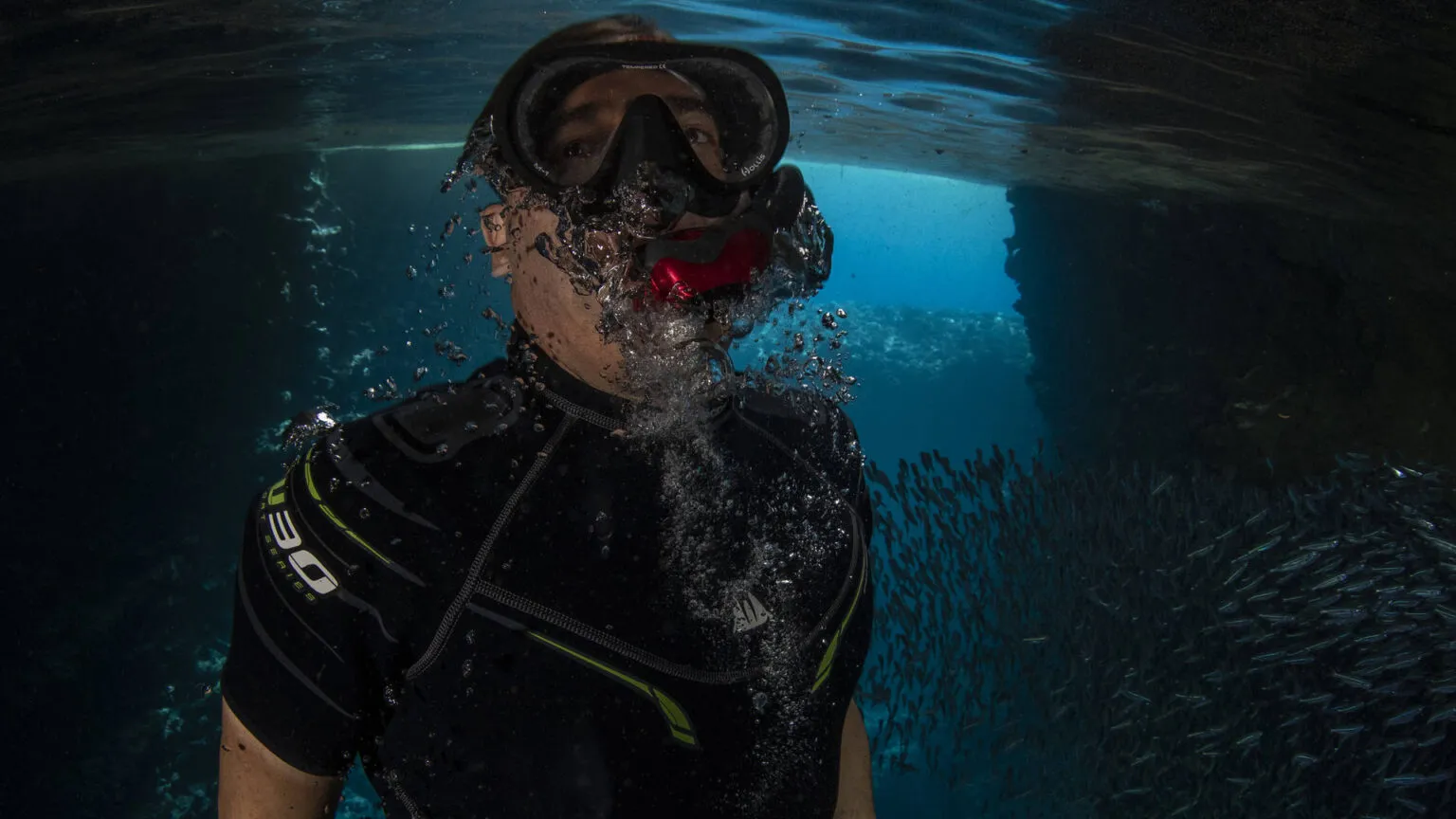 Een duiker met duikbril en snorkel bevindt zich net onder het wateroppervlak in de helderblauwe oceaan.