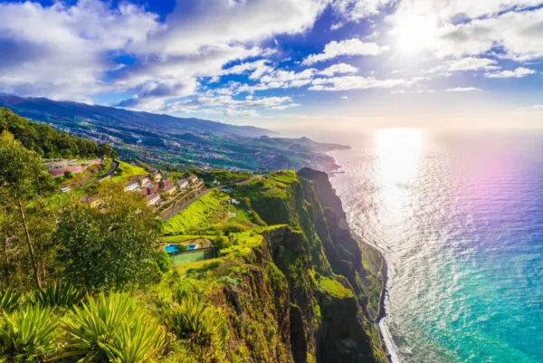 Panoramisch zicht vanaf de hoge, groene kliffen van Cabo Girão op de oceaan en de kustlijn van Madeira bij zonlicht.