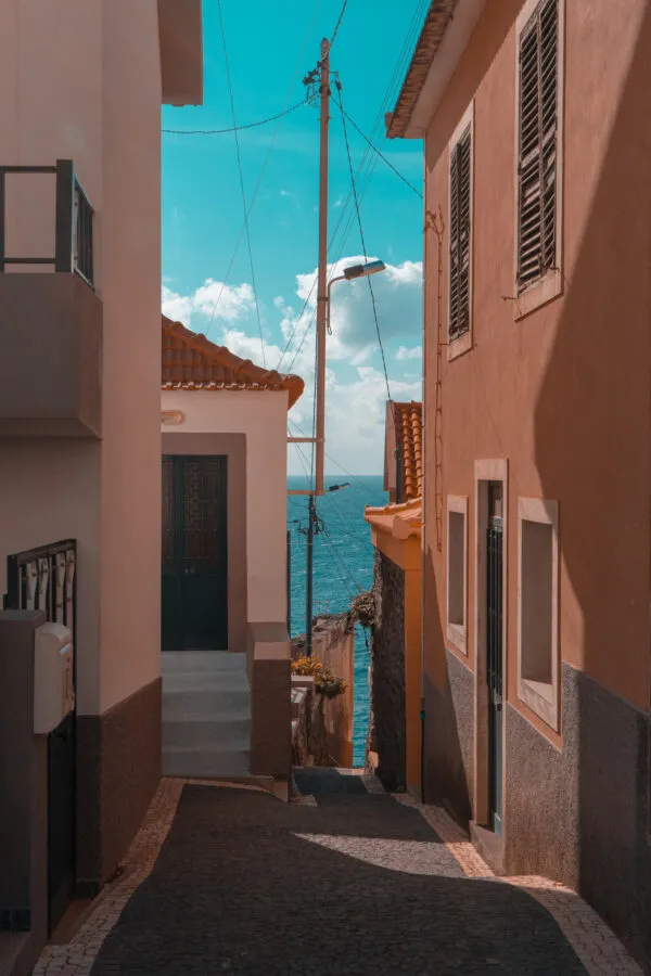 Een smal, hellend straatje tussen traditionele huizen in Funchal met doorkijk naar de blauwe oceaan op Madeira.
