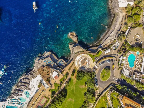 Lucht- en bovenaanzicht van de kust van Funchal met een kronkelende boulevard, een groen park en de heldere blauwe oceaan op Madeira.