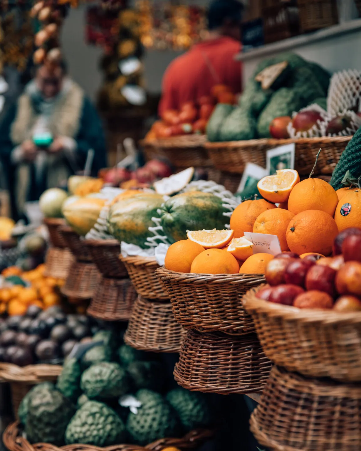 Gevlochten manden gevuld met vers exotisch fruit, zoals sinaasappels en passievruchten, op een kleurrijke marktkraam in Funchal op Madeira