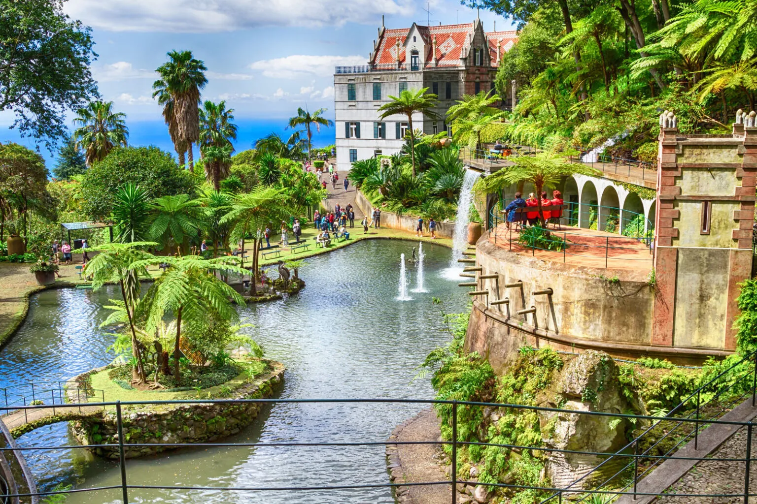 Grote vijver met fonteinen en een waterval, omgeven door weelderige tropische palmen en het historische Monte Palace paleis in Funchal op Madeira