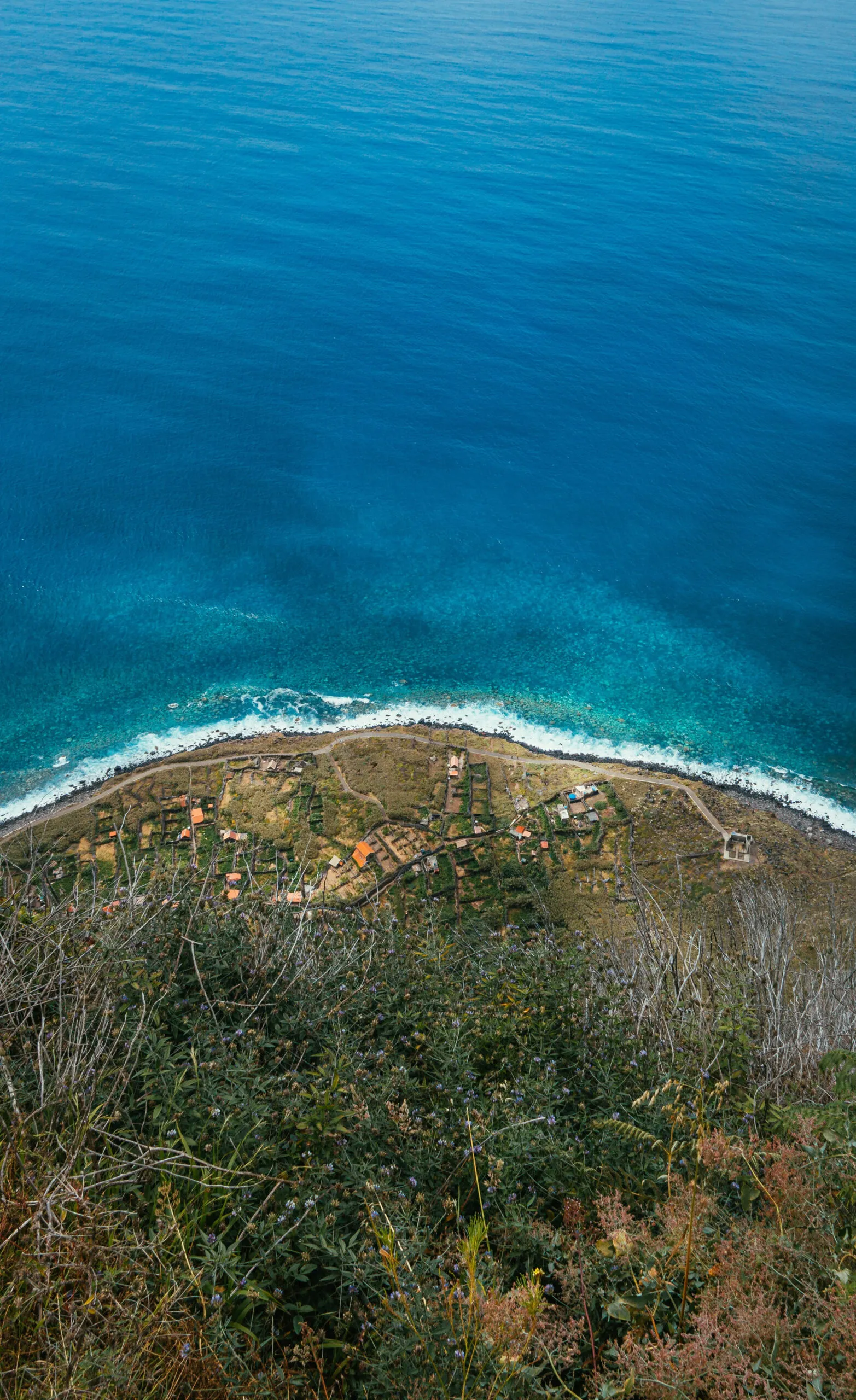 Loodrecht perspectief van bovenaf op de groene kliffen, het strand en de heldere, turquoise oceaan langs de kust bij Cabo Girão op Madeira.