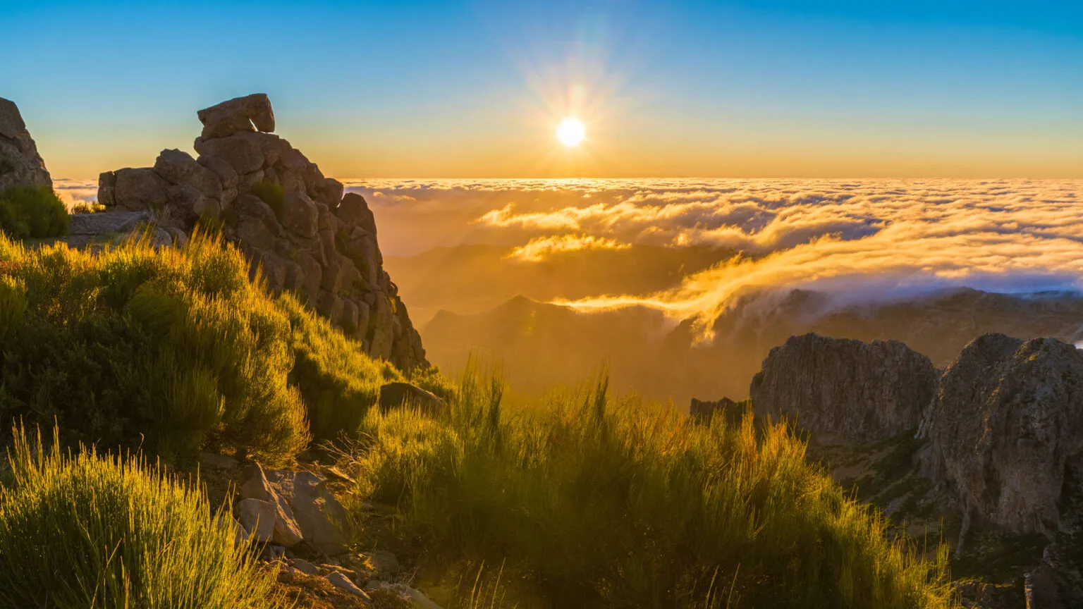 Een gouden zonsopgang boven een dicht wolkendek, gezien vanaf de bergtoppen tussen Pico do Arieiro en Pico Ruivo op Madeira.