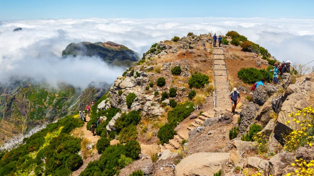 Wandelaars klimmen via een stenen trappenpad over een ruige bergkam boven het wolkendek bij Pico do Arieiro op Madeira