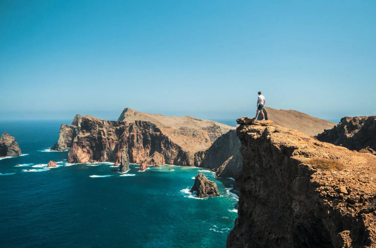 Reiziger staat op de rand van een steile klif met uitzicht op vulkanische rotsformaties en de oceaan bij Ponta de São Lourenço op Madeira